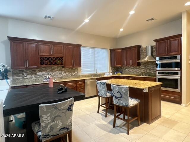 kitchen featuring light tile patterned floors, a kitchen island, stainless steel appliances, and wall chimney range hood