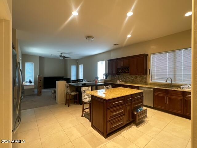 kitchen with stainless steel appliances, a center island, light stone countertops, sink, and ceiling fan