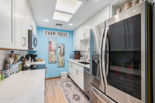 kitchen with stainless steel appliances, a sink, visible vents, white cabinetry, and tasteful backsplash