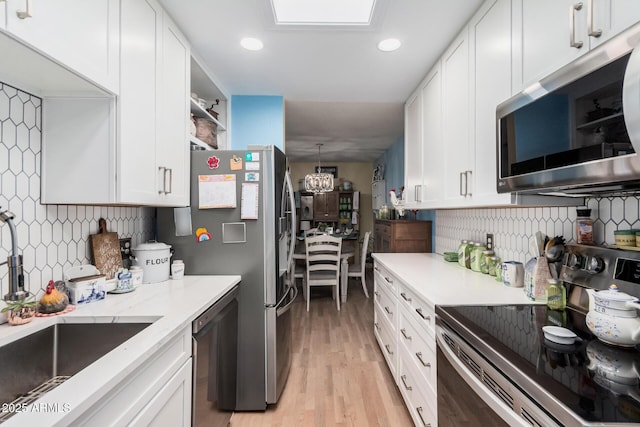 kitchen featuring light wood-style flooring, a sink, white cabinetry, appliances with stainless steel finishes, and tasteful backsplash