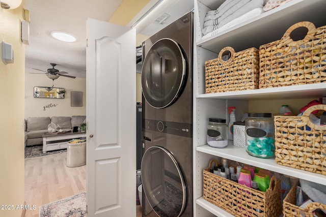 laundry room with laundry area, wood finished floors, visible vents, a ceiling fan, and stacked washer / drying machine