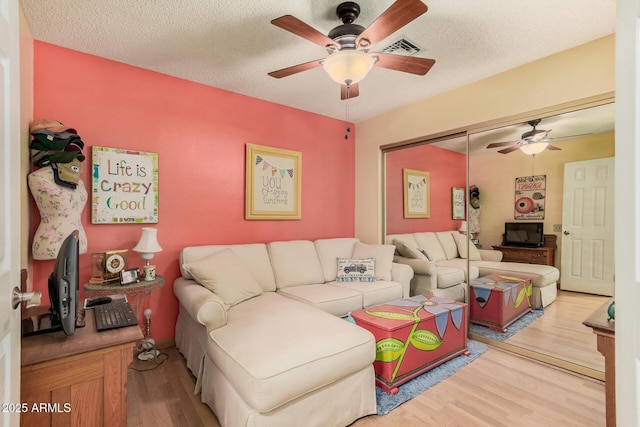 living area with light wood-style flooring, visible vents, ceiling fan, and a textured ceiling