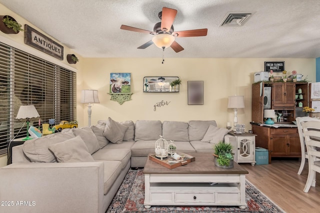 living room with a textured ceiling, wood finished floors, visible vents, and a ceiling fan