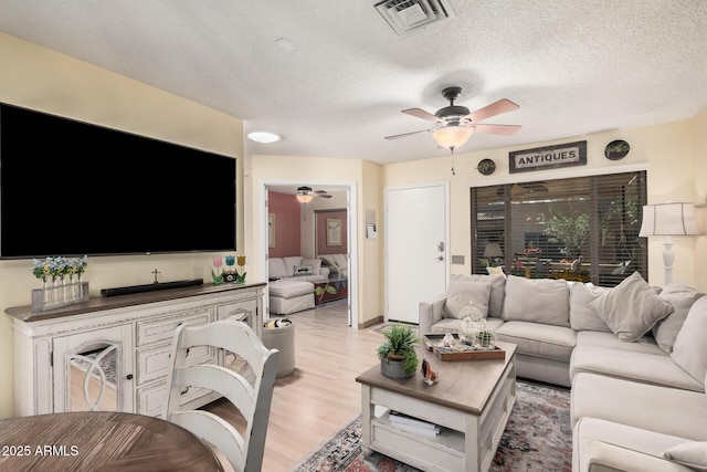 living area with a ceiling fan, light wood-type flooring, visible vents, and a textured ceiling