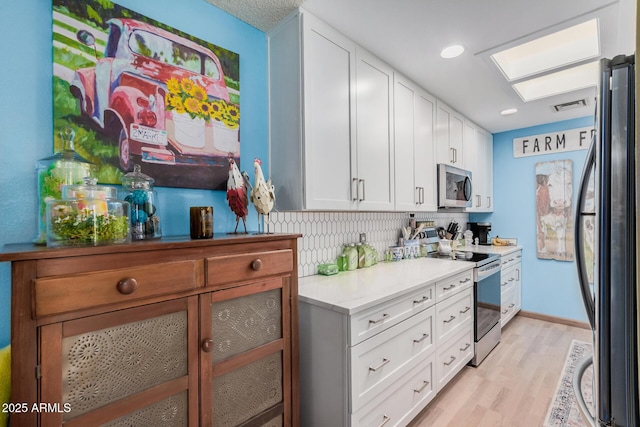 kitchen with stainless steel appliances, light countertops, visible vents, light wood-style floors, and white cabinetry