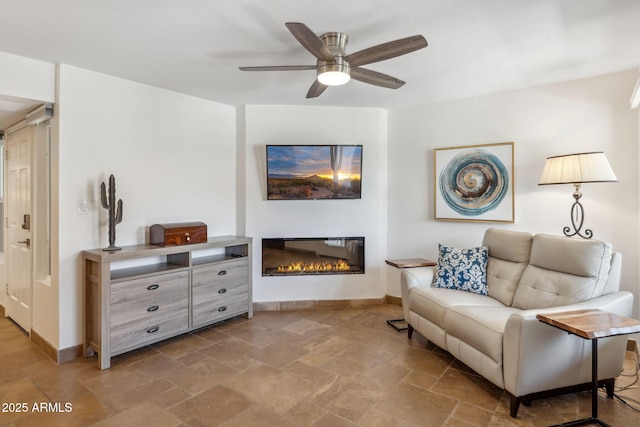 8787 E Mountain View Rd Unit 1100, Scottsdale, AZ 85258 - living room featuring a glass covered fireplace, stone tile floors, baseboards, and a ceiling fan