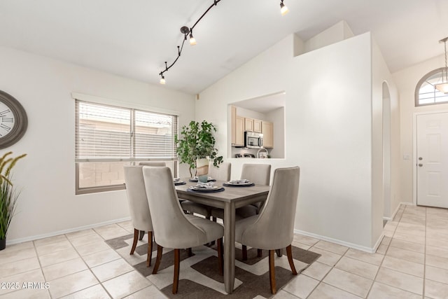 dining space with light tile patterned flooring, arched walkways, rail lighting, vaulted ceiling, and baseboards