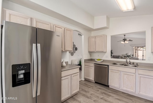 kitchen featuring appliances with stainless steel finishes, a sink, a ceiling fan, light brown cabinetry, and light wood-type flooring