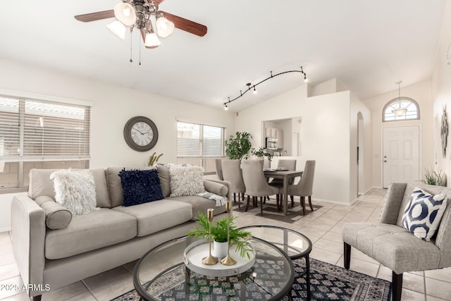 living area featuring a ceiling fan, vaulted ceiling, light tile patterned flooring, arched walkways, and baseboards