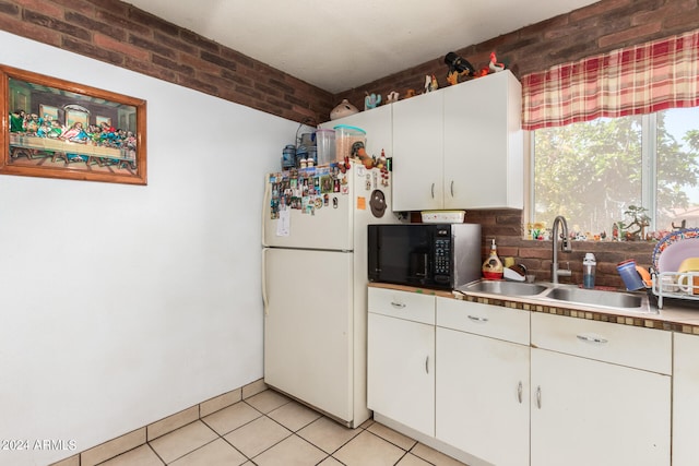 kitchen featuring brick wall, sink, white refrigerator, and white cabinetry