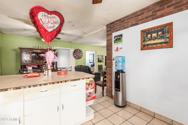 kitchen featuring white cabinets, ceiling fan, light tile floors, and brick wall