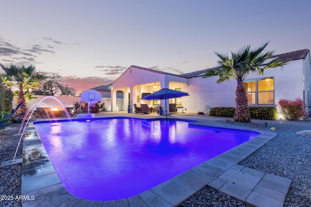 pool at dusk with a patio and pool water feature