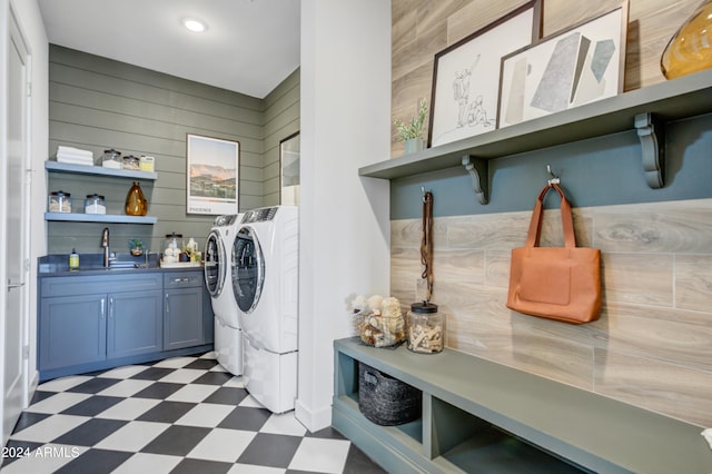 laundry area featuring wooden walls, washing machine and clothes dryer, cabinets, and sink