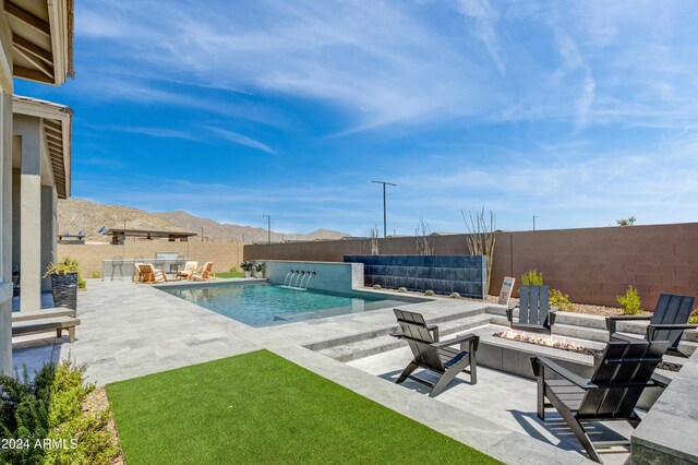 view of swimming pool with a fire pit, pool water feature, a mountain view, and a patio