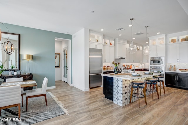 kitchen featuring an island with sink, custom exhaust hood, appliances with stainless steel finishes, and light hardwood / wood-style floors