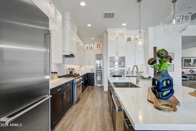 kitchen with white cabinets, high end appliances, decorative light fixtures, light hardwood / wood-style floors, and tasteful backsplash