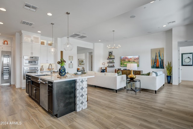 kitchen with decorative light fixtures, light hardwood / wood-style floors, a kitchen island with sink, sink, and white cabinetry