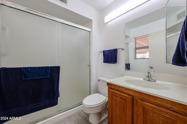 bathroom featuring hardwood / wood-style floors, a shower with shower door, vanity, and toilet