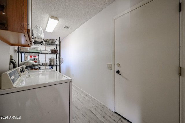 laundry area featuring cabinets, light hardwood / wood-style flooring, washer and dryer, and a textured ceiling