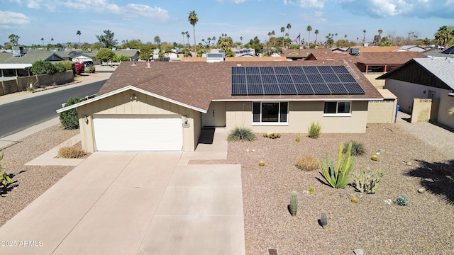 ranch-style home with a garage, solar panels, a shingled roof, concrete driveway, and a residential view