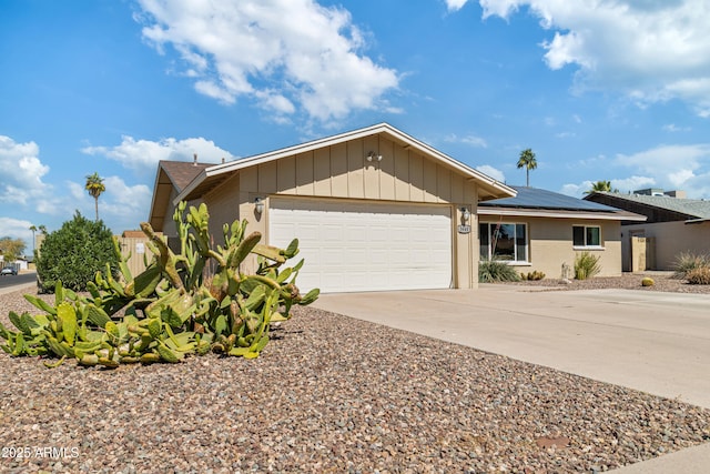 ranch-style house featuring an attached garage, board and batten siding, solar panels, and concrete driveway