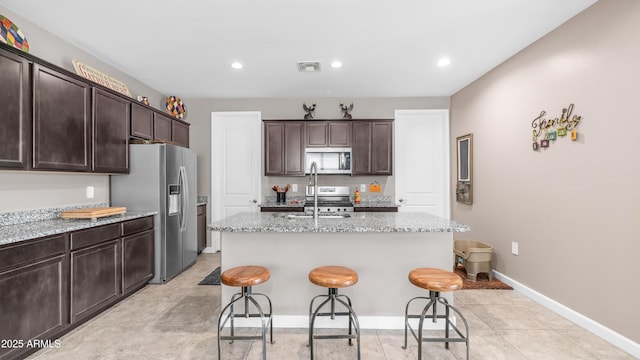 37820 W San Sisto Ave, Maricopa, AZ 85138 - kitchen featuring a sink, dark brown cabinetry, stainless steel appliances, a kitchen bar, and light stone countertops