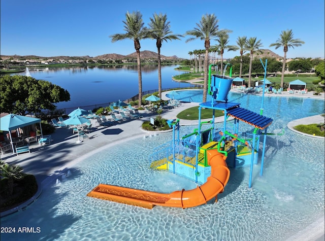 view of swimming pool with a water slide, a playground, and a water and mountain view