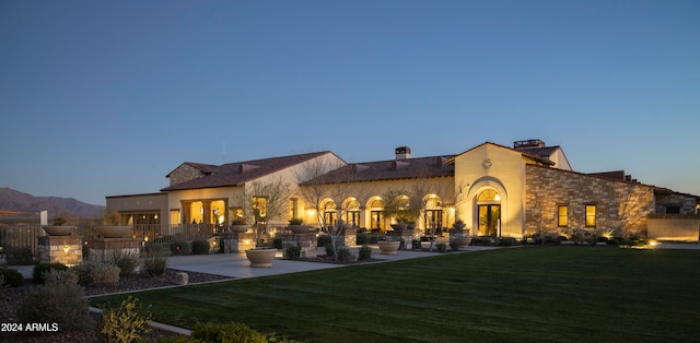 back house at dusk with a patio, a mountain view, and a lawn