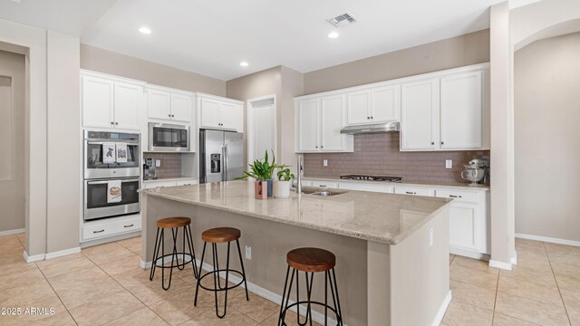 kitchen with a sink, under cabinet range hood, tasteful backsplash, visible vents, and appliances with stainless steel finishes