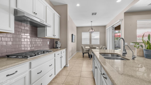 kitchen with a sink, under cabinet range hood, tasteful backsplash, visible vents, and baseboards