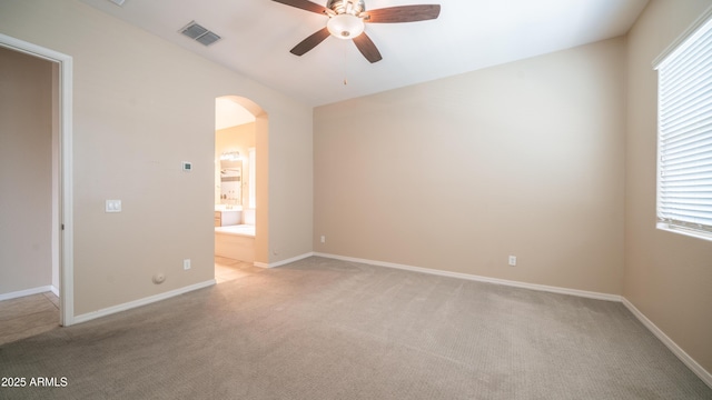 spare room featuring a wealth of natural light, a ceiling fan, visible vents, light carpet, and arched walkways