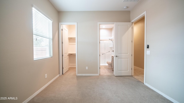 unfurnished bedroom with baseboards, light colored carpet, a closet, a walk in closet, and visible vents