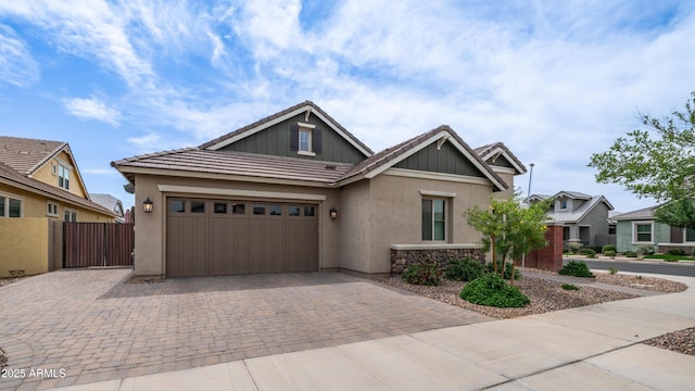 craftsman-style home featuring stucco siding, decorative driveway, fence, and a garage