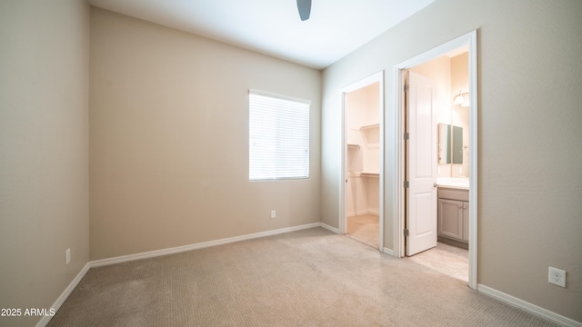 unfurnished bedroom featuring a closet, ensuite bath, a walk in closet, baseboards, and light colored carpet