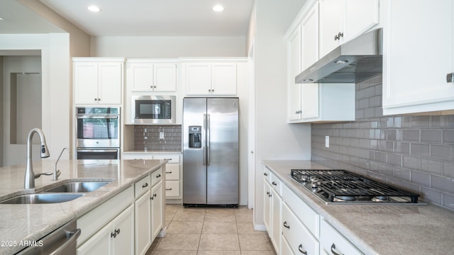kitchen with a sink, stainless steel appliances, under cabinet range hood, tasteful backsplash, and white cabinetry