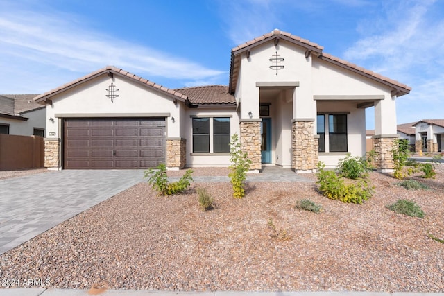 mediterranean / spanish-style home featuring an attached garage, driveway, stone siding, a tiled roof, and stucco siding