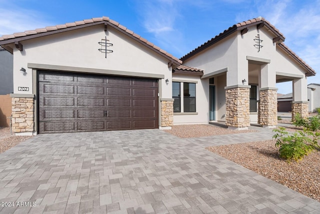 view of front facade with a garage, stone siding, decorative driveway, and stucco siding