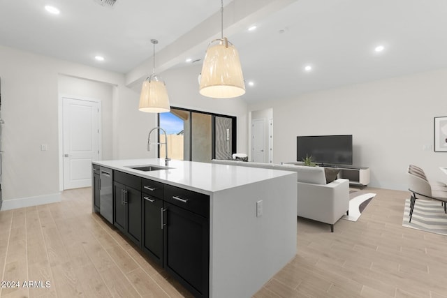 kitchen with an island with sink, light wood-style flooring, dark cabinets, light countertops, and a sink