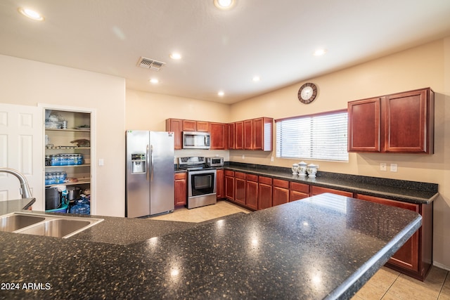 kitchen featuring appliances with stainless steel finishes, light tile patterned floors, dark stone counters, and sink