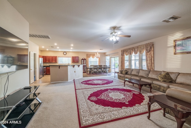 living room with ceiling fan with notable chandelier and light colored carpet