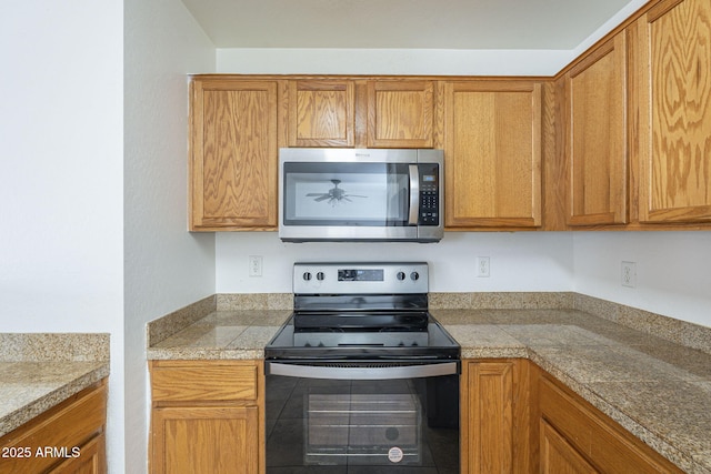 kitchen featuring tile countertops, electric range, stainless steel microwave, and brown cabinetry