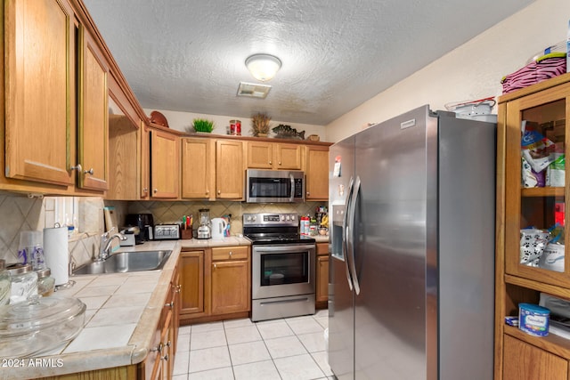 kitchen featuring tile counters, sink, tasteful backsplash, light tile patterned flooring, and appliances with stainless steel finishes