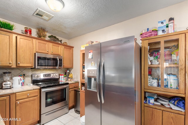 kitchen with light tile patterned flooring, backsplash, appliances with stainless steel finishes, a textured ceiling, and tile countertops