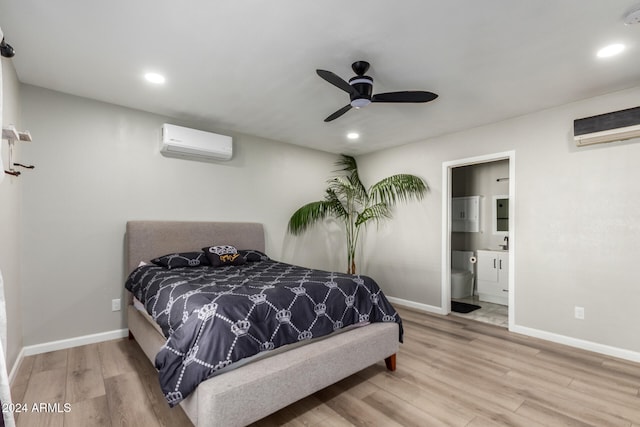 bedroom featuring light hardwood / wood-style flooring, ceiling fan, ensuite bath, and a wall mounted air conditioner