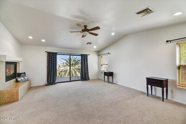 living room with plenty of natural light, light colored carpet, lofted ceiling, and a tiled fireplace