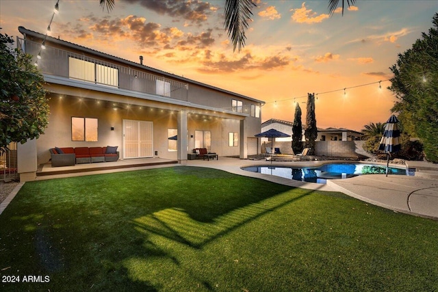 back house at dusk with an outdoor living space, a patio area, and a yard