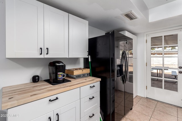 kitchen featuring light tile patterned floors, visible vents, white cabinets, butcher block countertops, and black refrigerator with ice dispenser