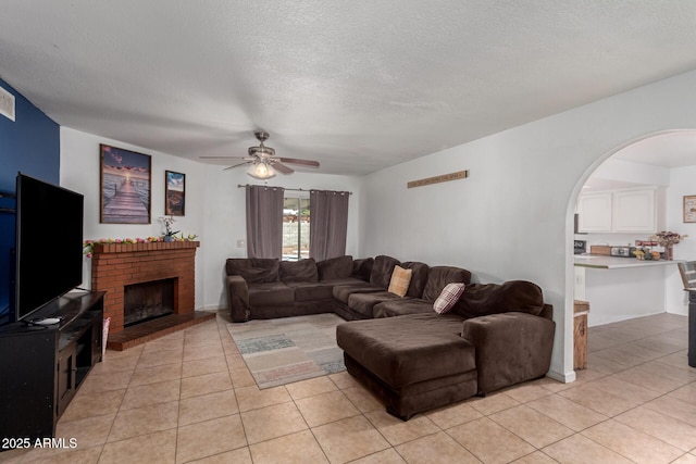 living area with light tile patterned floors, a textured ceiling, a brick fireplace, and arched walkways