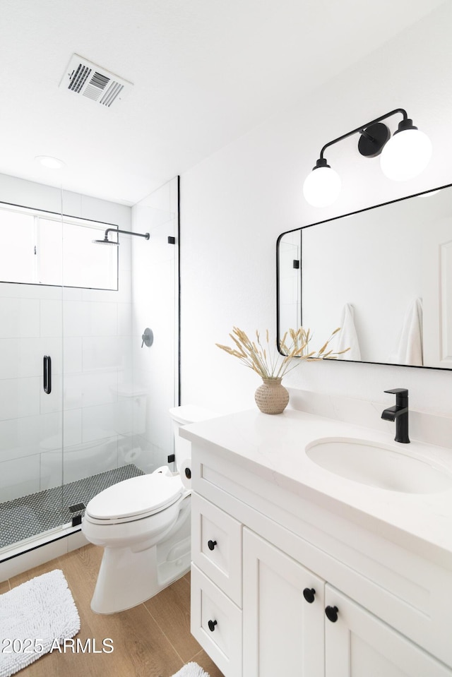 bathroom featuring visible vents, toilet, a shower stall, vanity, and wood finished floors