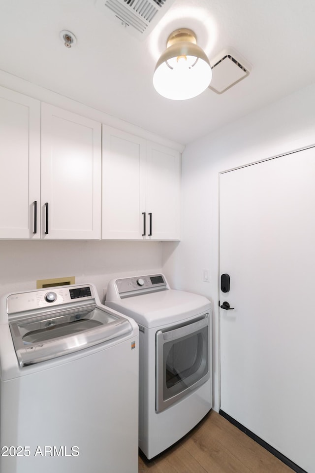 laundry area featuring visible vents, wood finished floors, washing machine and clothes dryer, and cabinet space